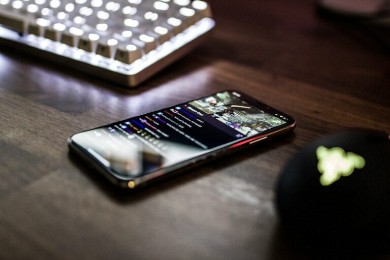 Smartphone on a wooden desk showing a Twitch stream with chat, a backlit keyboard behind it